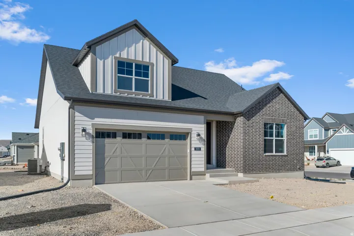 Two-car garage with overhead door, concrete driveway, board and batten siding, brick facade, and dark shingle roof