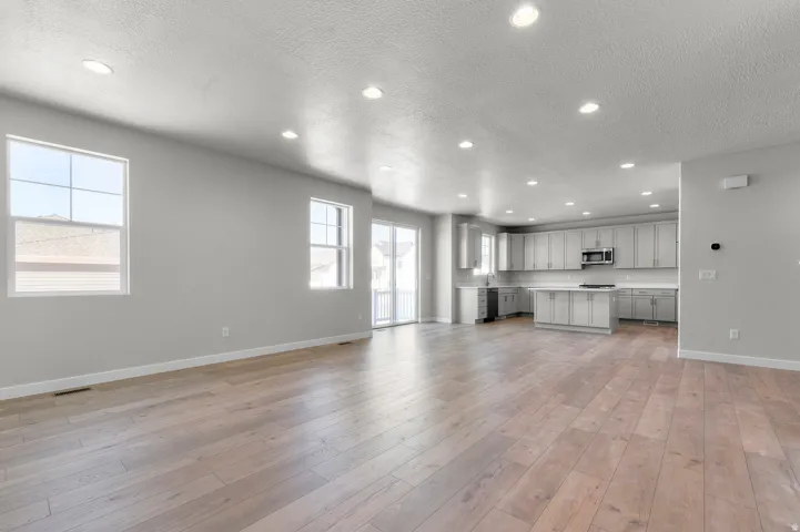 Bright, open-concept living area featuring recessed ceiling lighting, expansive wood-finish flooring throughout, and abundant natural light from multiple windows and glass doors