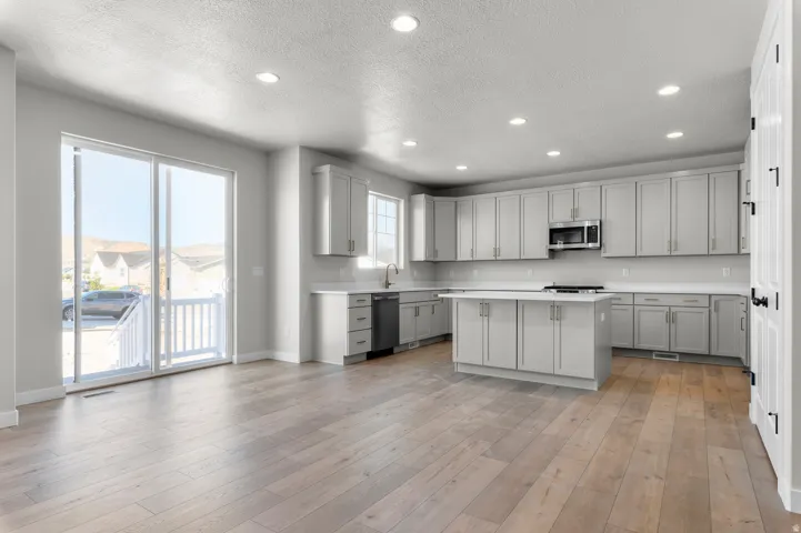 Open concept living space featuring wood-finish flooring, a kitchen island, recessed lighting, and a sliding glass door with a balcony