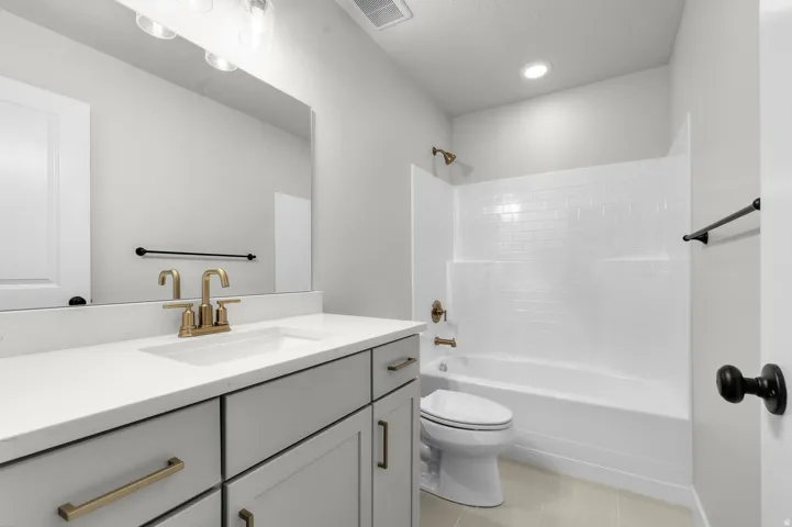 Vanity with light gray cabinetry, white countertop, and gold-finish hardware