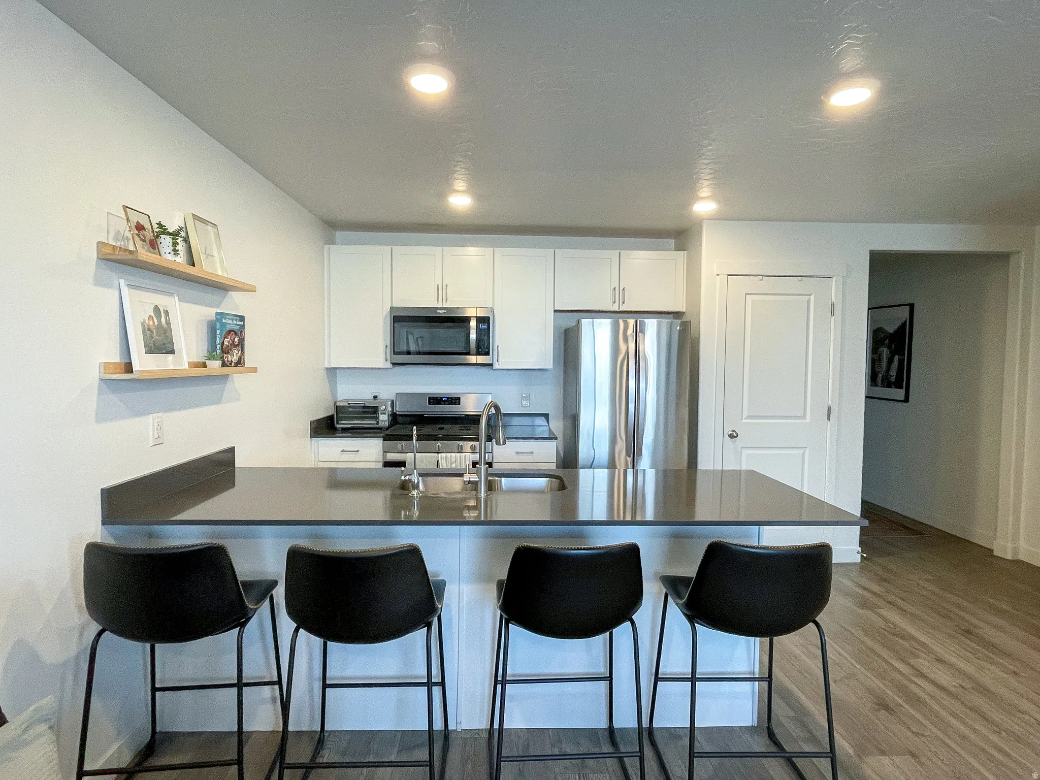 Kitchen featuring white cabinetry, stainless steel appliances, a dark countertop island with seating, and recessed lighting