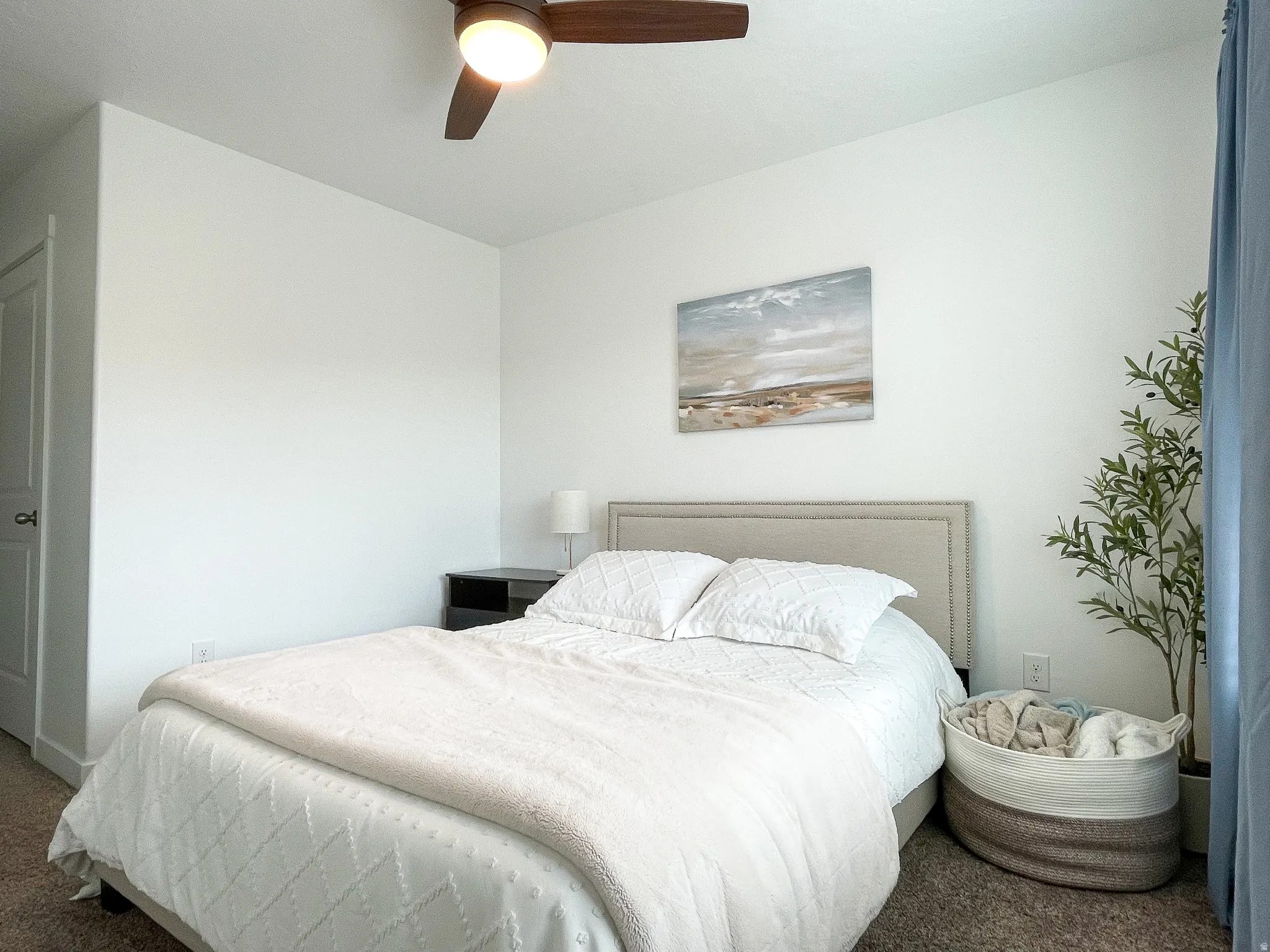Carpeted bedroom featuring a dark wood-finish ceiling fan with integrated lighting, a neutral upholstered headboard, and a built-in closet with a white door