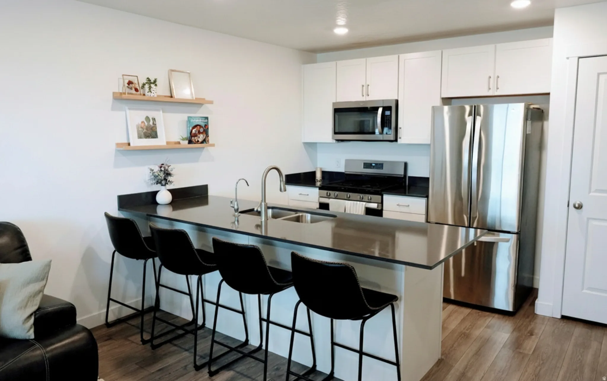 Modern kitchen featuring an island with a breakfast bar, stainless steel appliances, white cabinetry, dark countertops, and wood-finish flooring