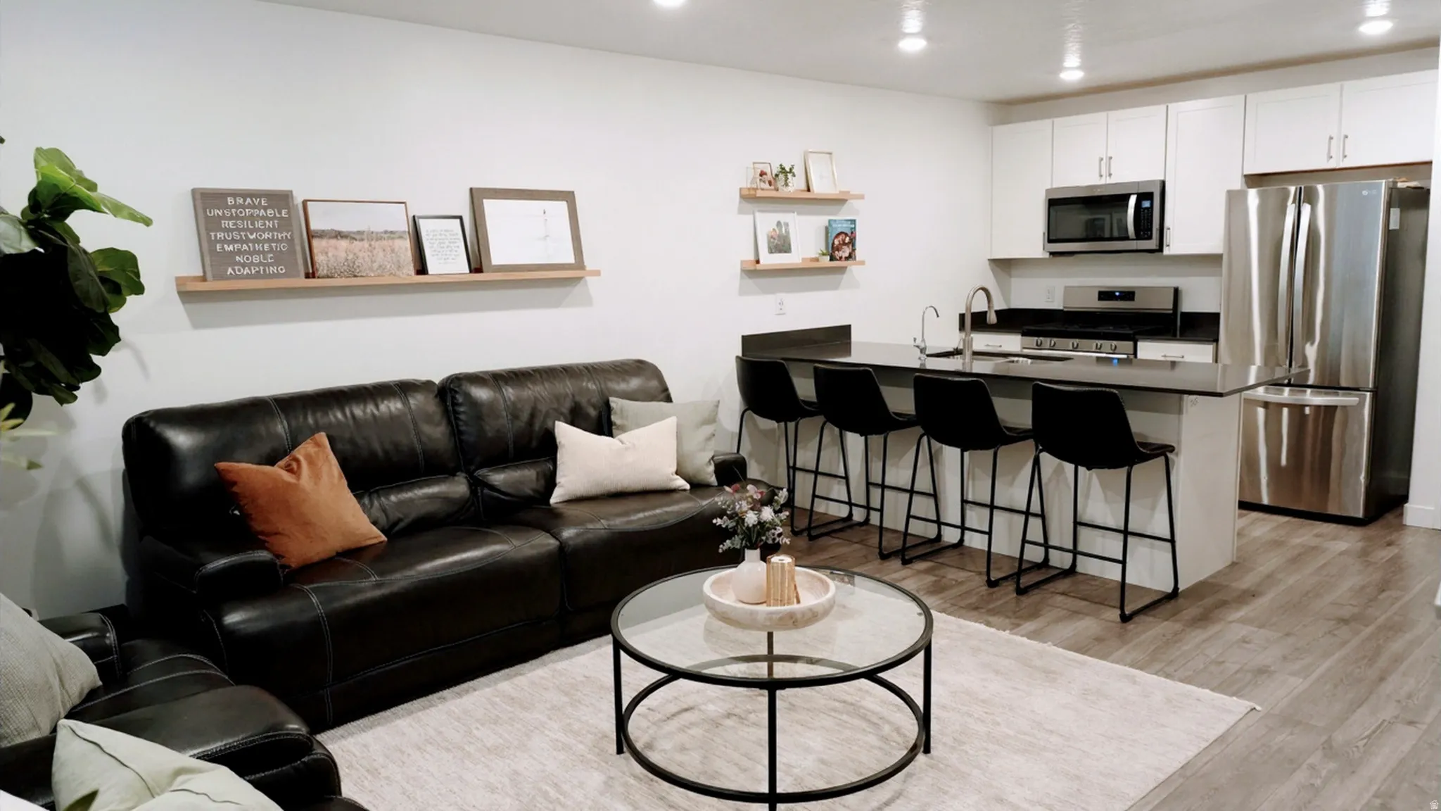 Open-concept living space featuring wood-finish flooring, a contemporary kitchen with white cabinetry, stainless steel appliances, a dark countertop, and an extended island with seating