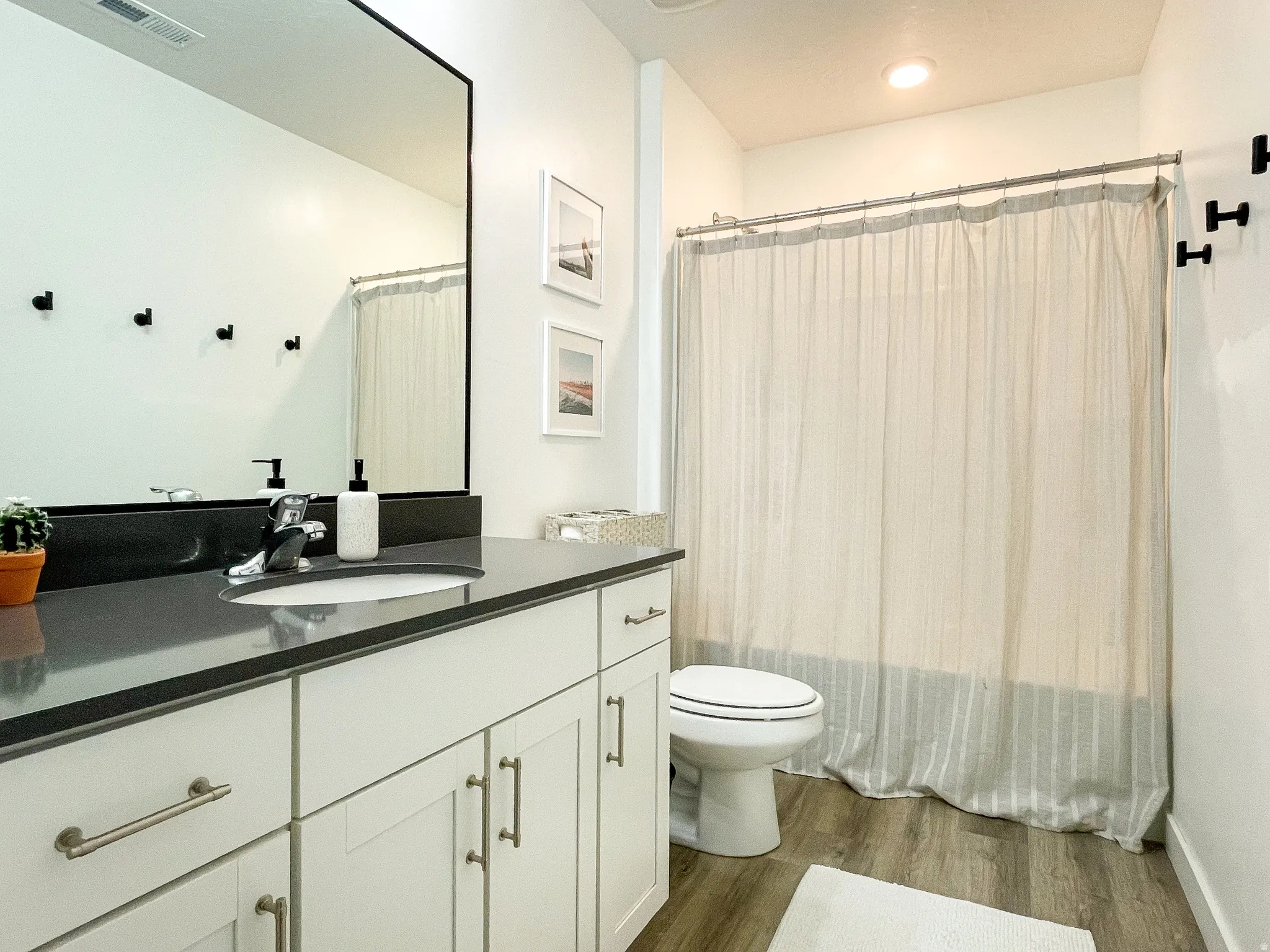 Bathroom featuring a white vanity with brushed nickel hardware, a dark countertop, an integrated sink with a chrome faucet, and wood-finish flooring