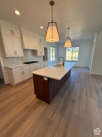 Spacious kitchen featuring white cabinetry, a large wood-finish island with a light-toned countertop, a tile backsplash, and stainless steel appliances