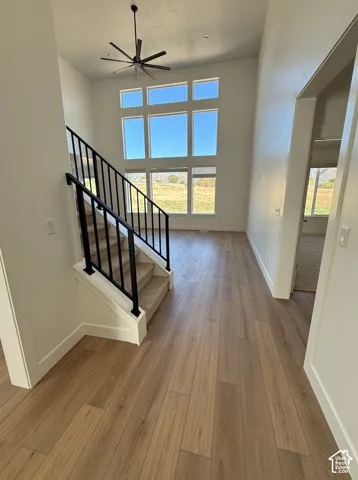 Two-story foyer with wood-finish flooring, a contemporary ceiling fan, and abundant natural light from multi-panel windows