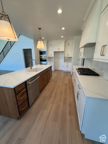 Gourmet kitchen with wood-finish flooring, white cabinetry, a large center island with a sink, stainless steel appliances, and quartz countertops