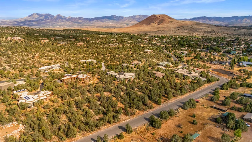 Expansive desert landscape featuring scattered residences and mature trees, with distant mountains and a prominent conical hill forming the horizon