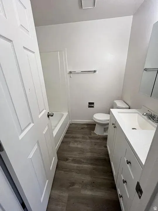 Contemporary bathroom featuring a white vanity with integrated sink, wood-finish flooring, a white bathtub with shower surround, a white toilet, and a medicine cabinet with mirrored door