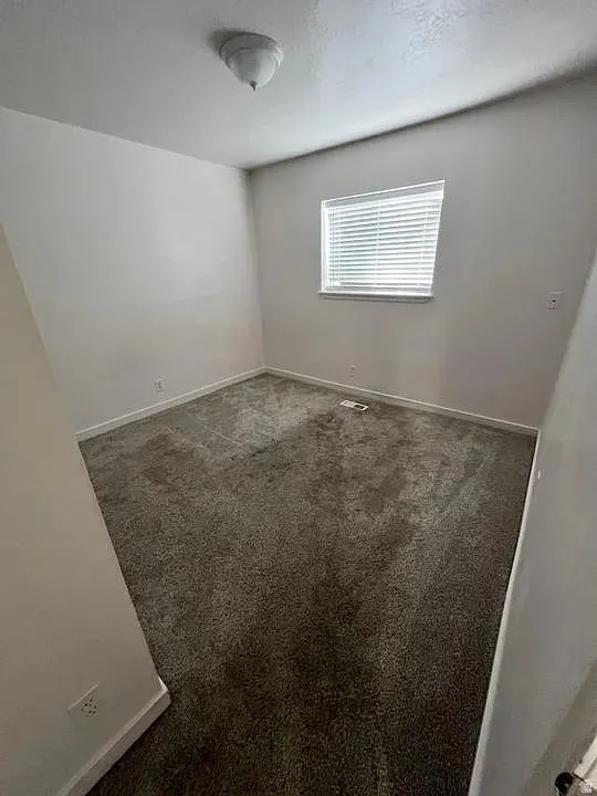 Carpeted room with a single window featuring horizontal blinds