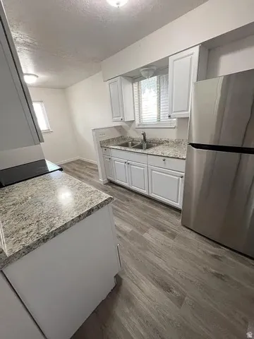 Kitchen featuring white shaker-style cabinetry, granite-look countertops, a double basin stainless steel sink with a chrome faucet, and wood-finish flooring