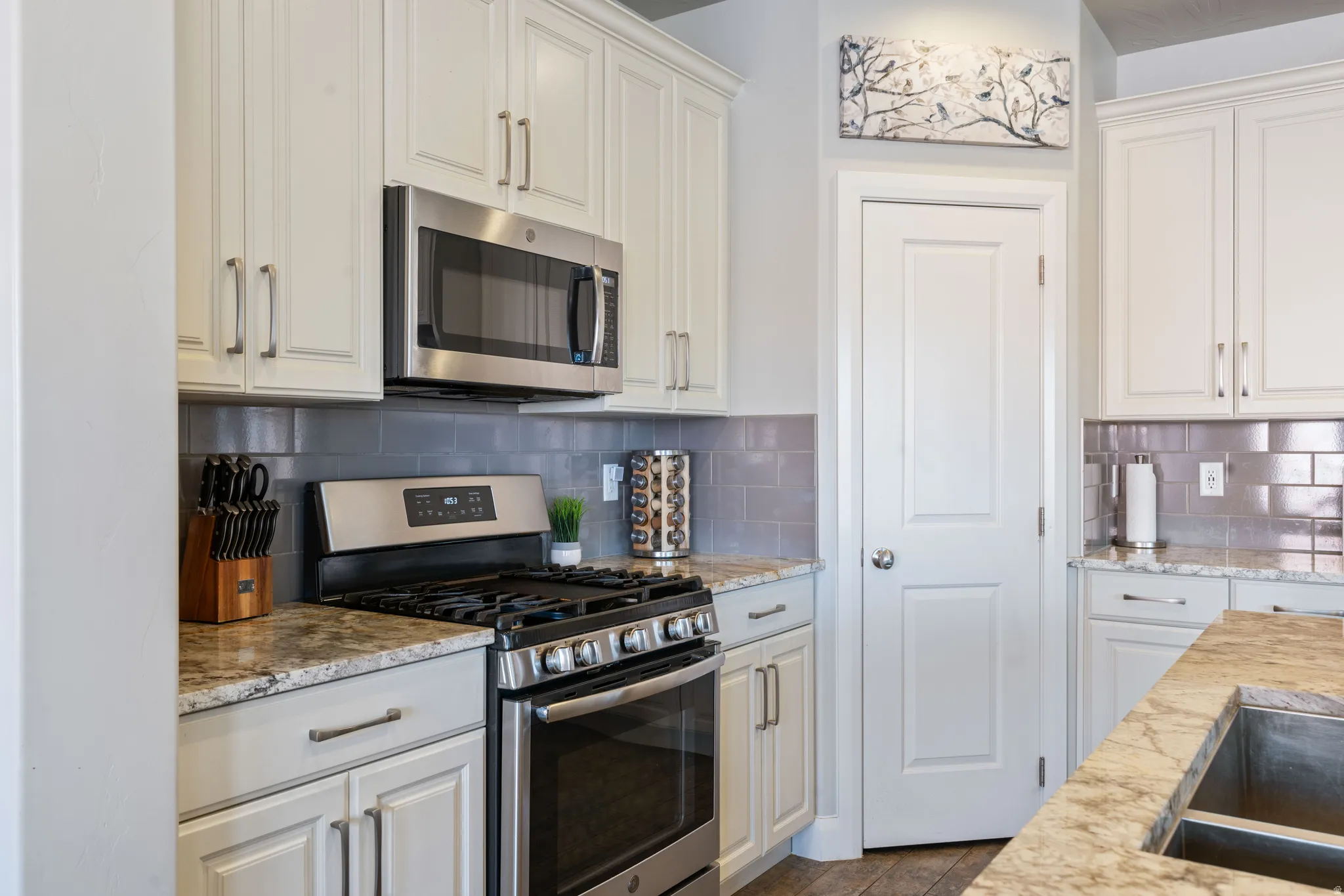 Well-appointed kitchen featuring a stainless steel gas range, coordinating stainless steel microwave, light-toned cabinetry, gray subway tile backsplash, and stone countertops