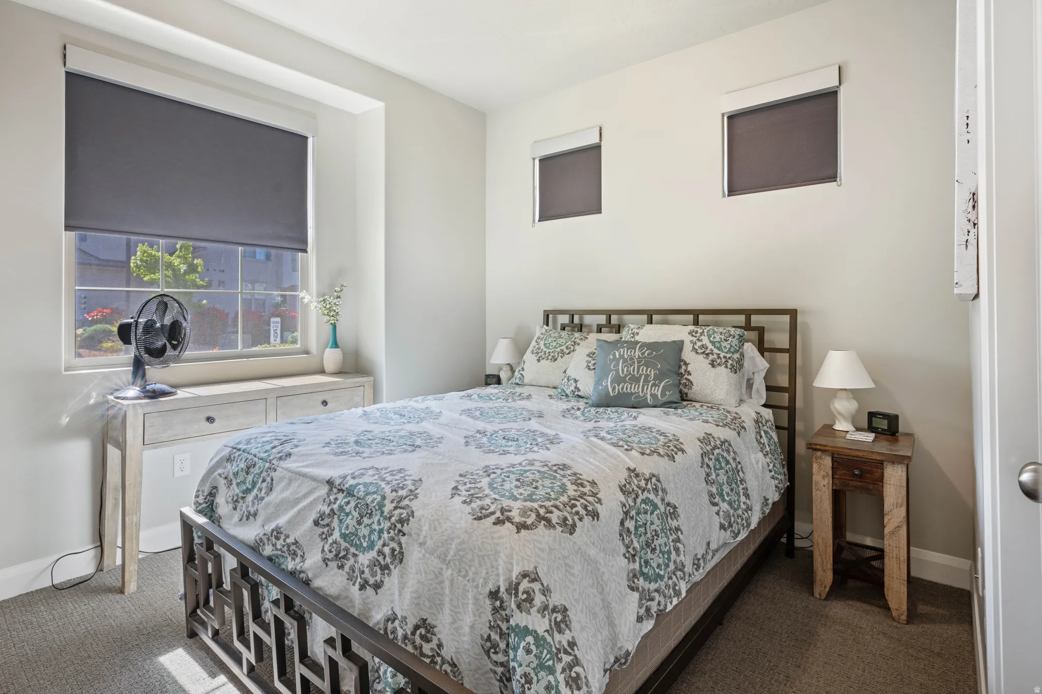 Carpeted bedroom featuring a large window with roller shade, two additional high windows with roller shades, and light-toned wall paint