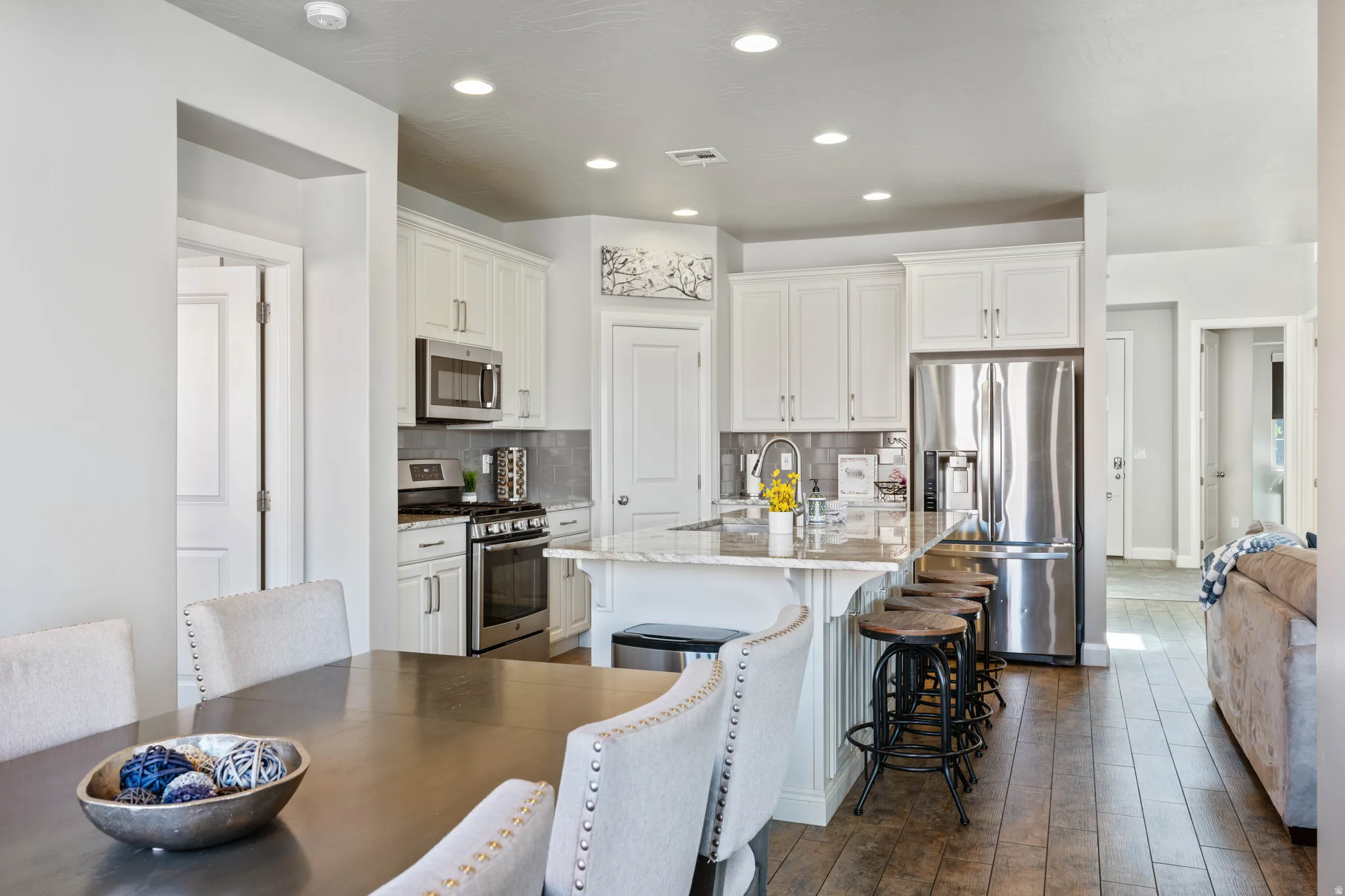 Open-concept kitchen featuring white cabinetry, stainless steel appliances, a multi-level island with seating, and wood-finish flooring