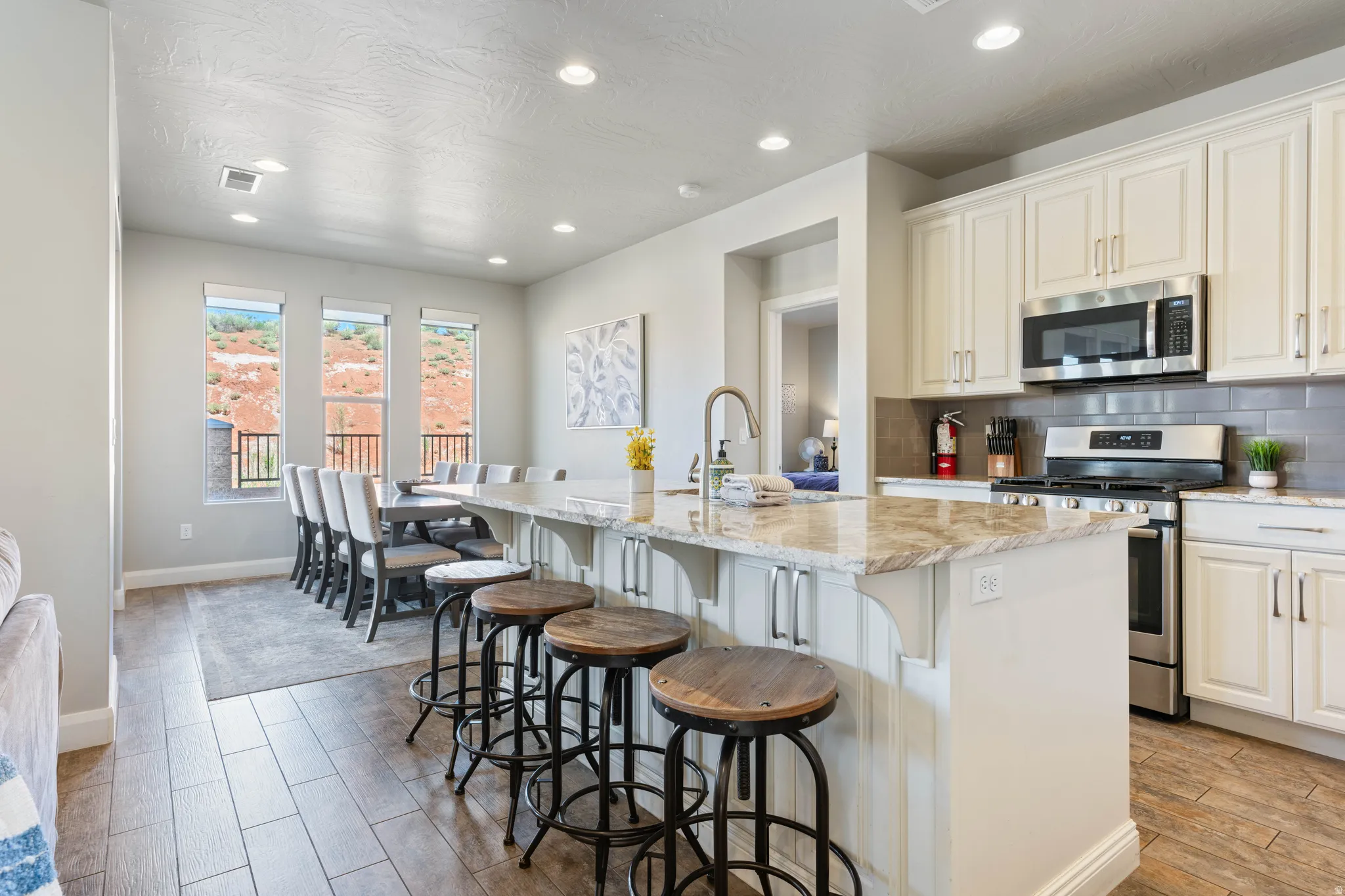 Open-concept kitchen and dining area featuring a spacious island with a stone countertop, white cabinetry, stainless steel appliances, and wood-finish flooring