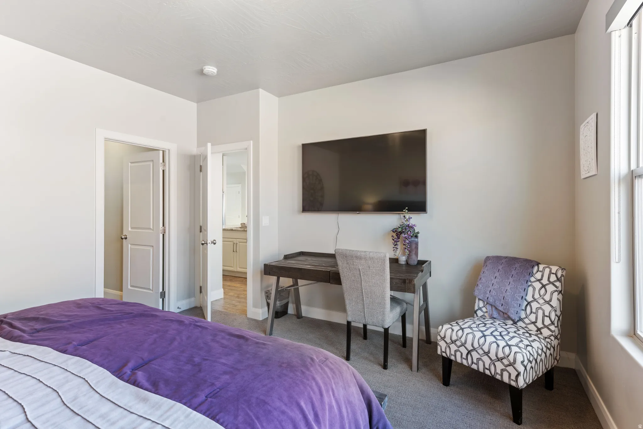 Bedroom featuring light gray walls, built-in wall-mounted television, and a window with blinds