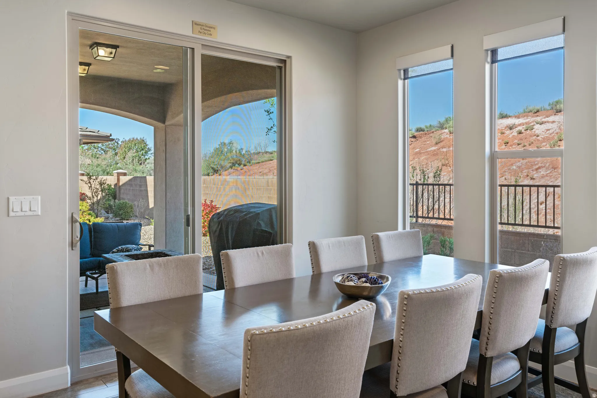 Bright dining area featuring a sliding glass door to an outdoor patio, multiple windows with desert scenery, and light-colored walls