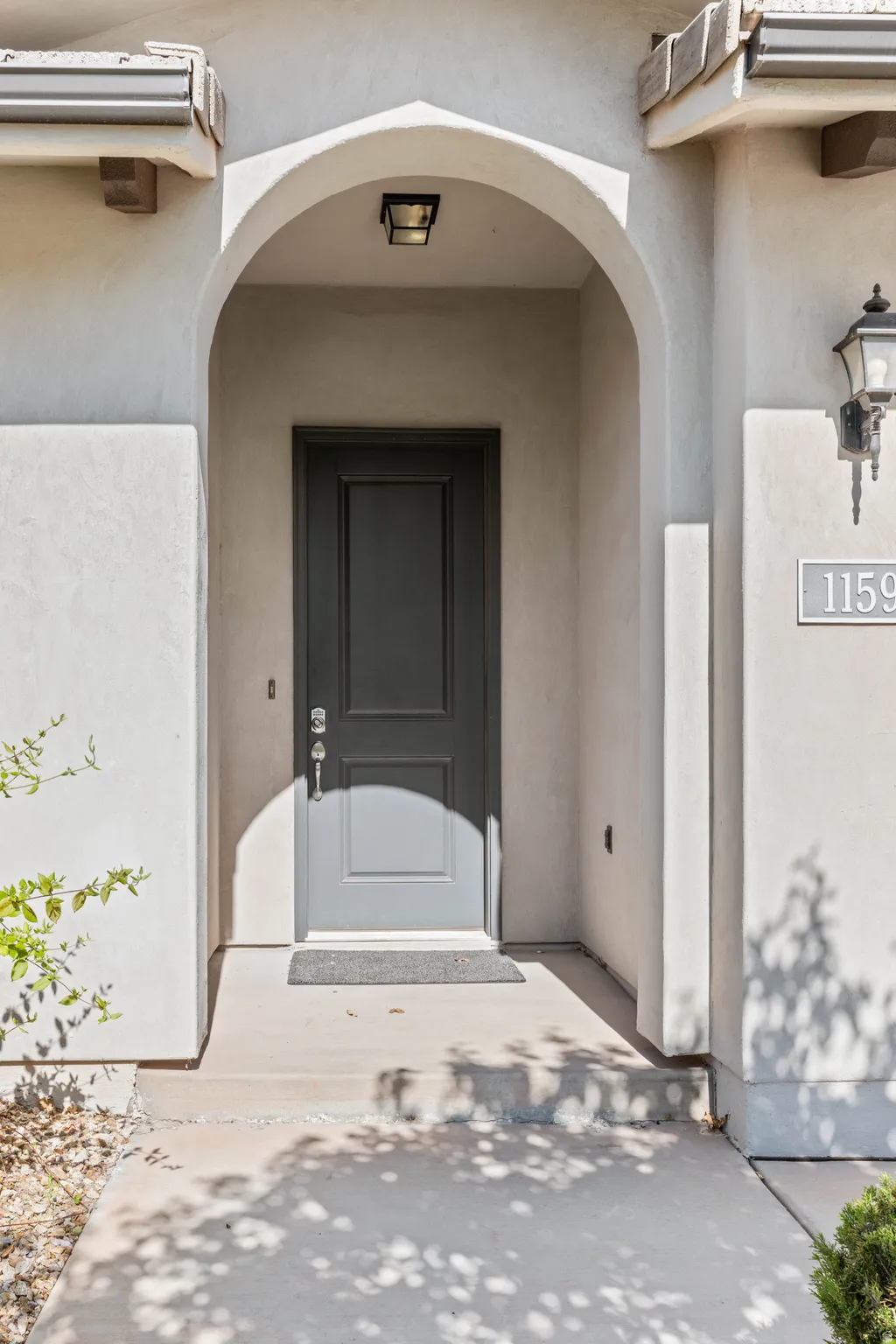 Arched entryway featuring a dark gray door with chrome hardware, an overhead flush-mount light fixture, and a stucco exterior finish