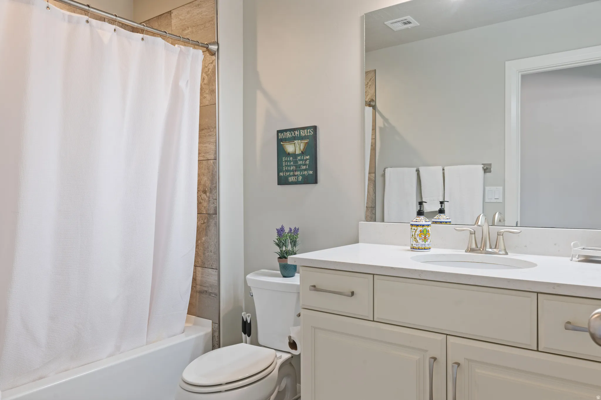 Bathroom featuring a tub/shower combination with natural stone-look tile surround, a white vanity with shaker-style cabinetry, and a light-colored countertop with an integrated sink