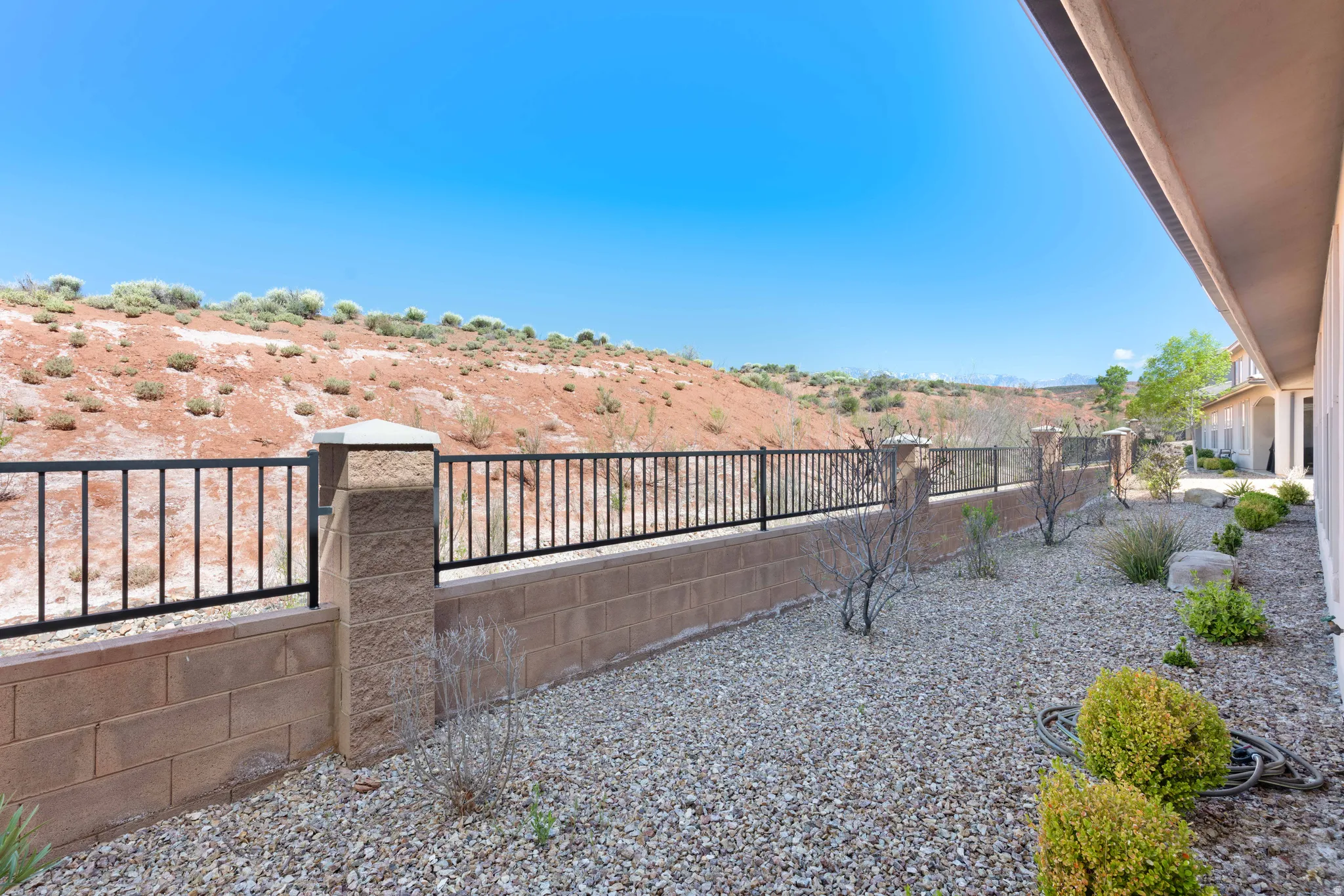 Landscaped backyard featuring gravel ground cover, low-maintenance plantings, and a block wall with wrought iron fencing