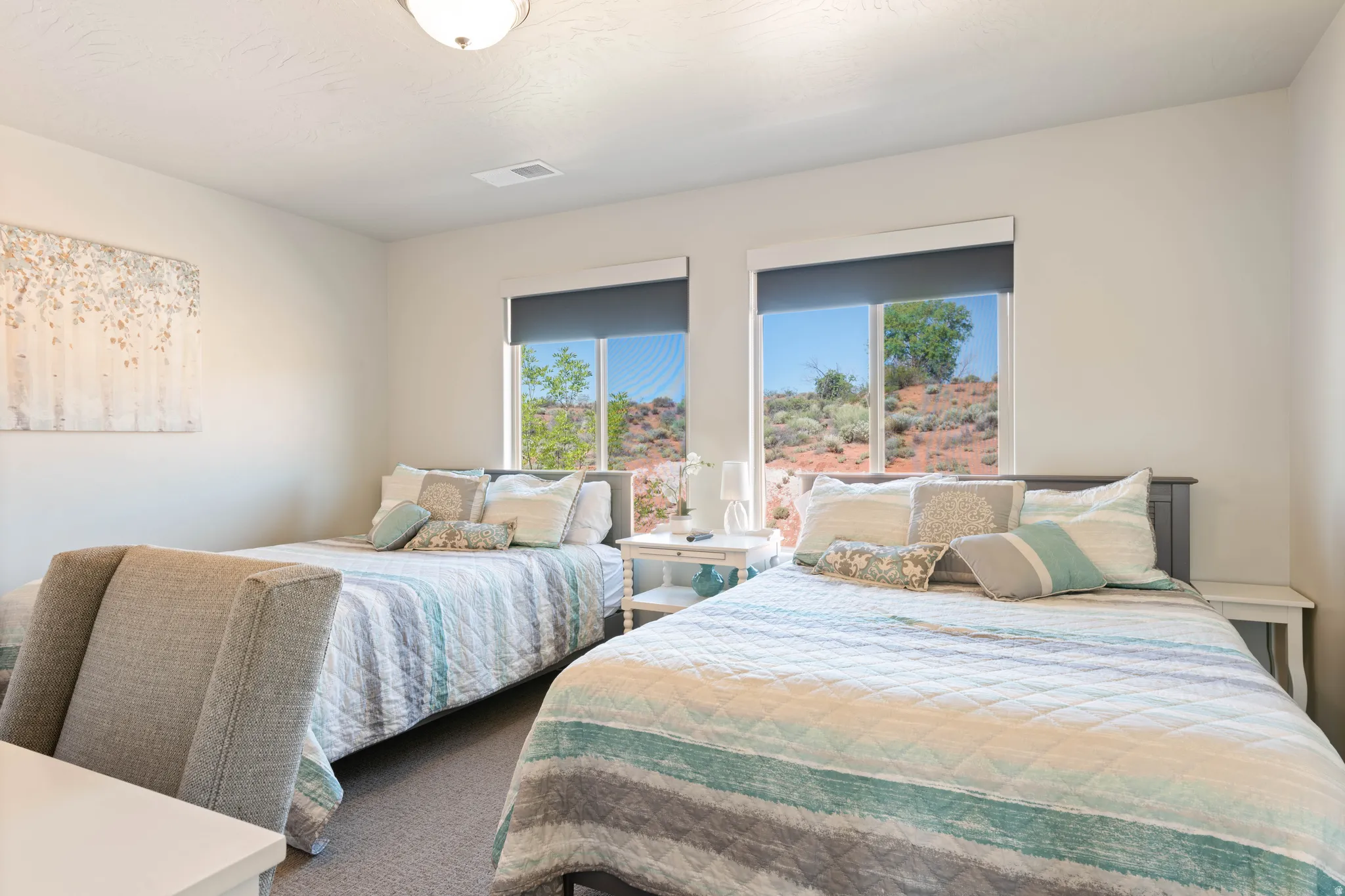 Bedroom featuring two beds with headboards, two windows with roller shades, and light-colored walls