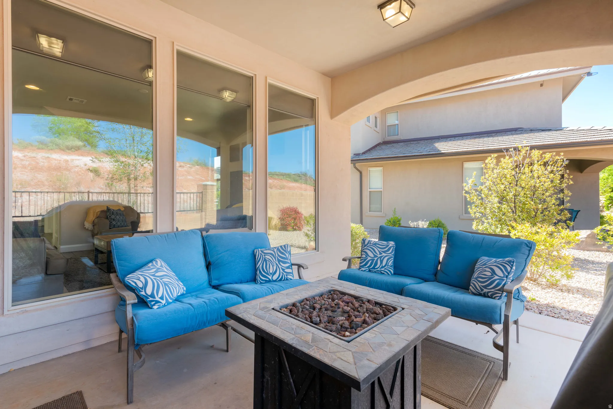 Covered patio featuring a fire pit with a stone-finish top, an arched entryway, recessed lighting, and large windows