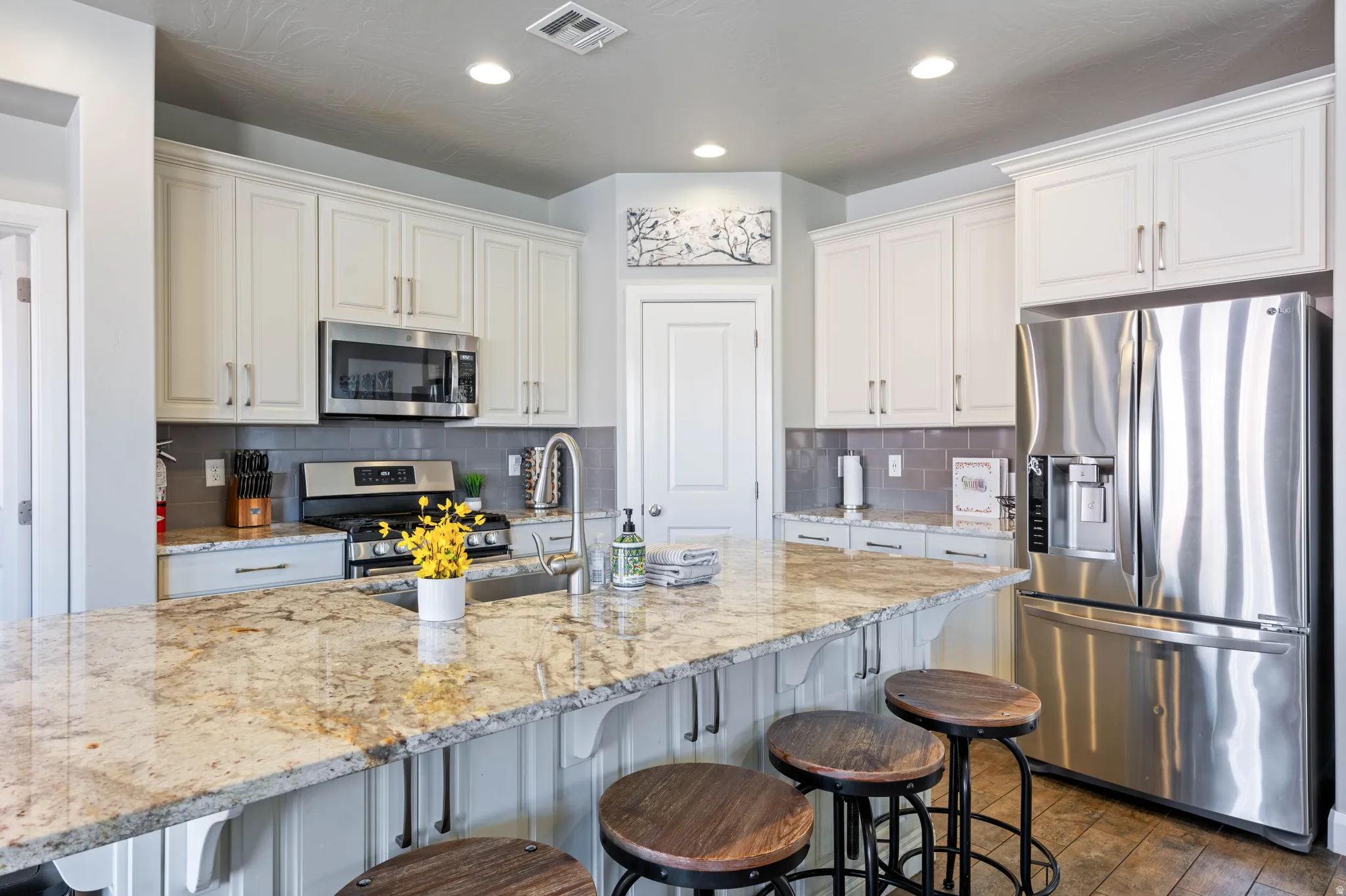 Kitchen featuring a large island with a stone countertop, stainless steel appliances, white cabinetry, and recessed lighting