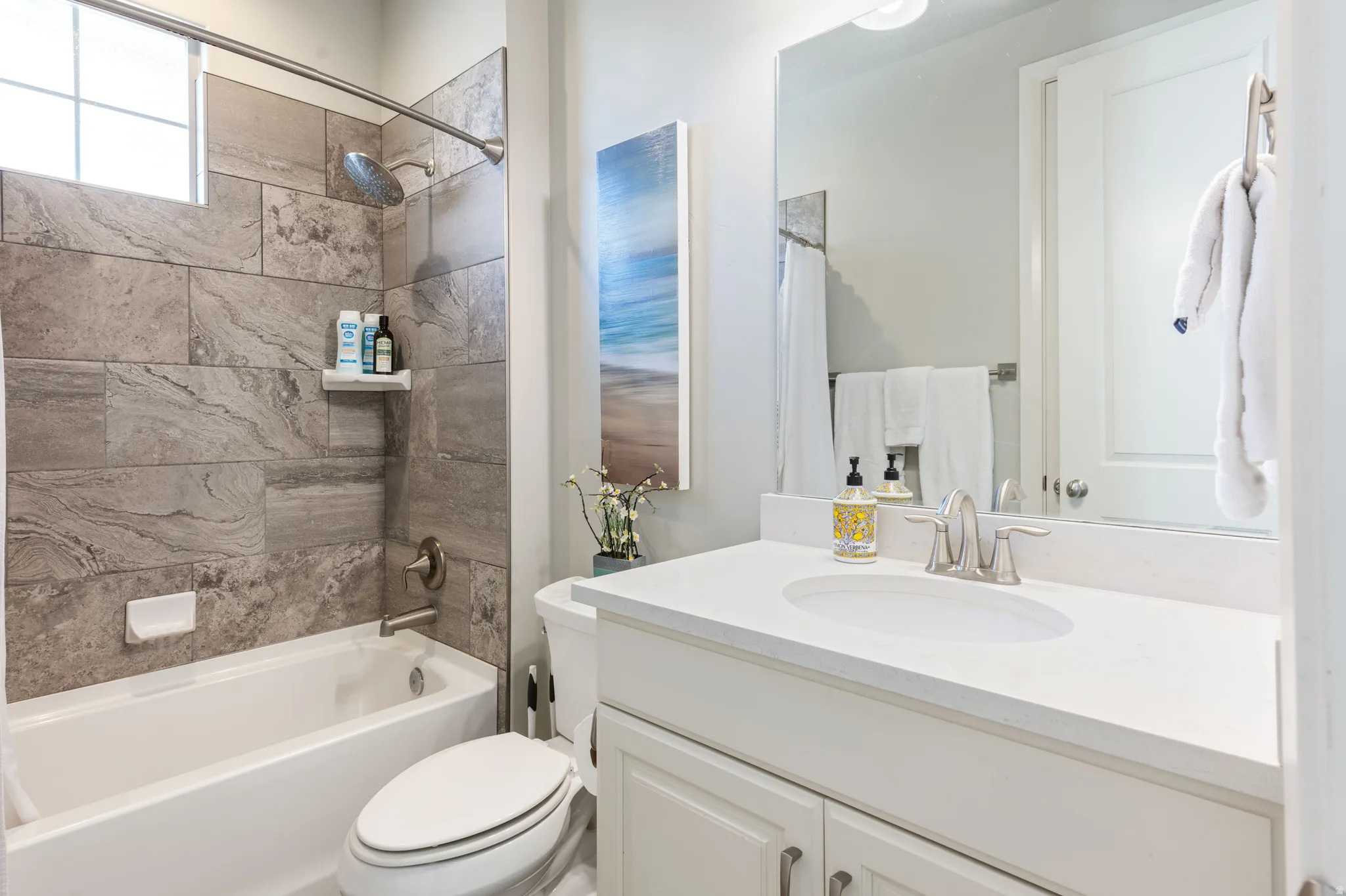 Full bathroom featuring a tub/shower combination with large format stone-look tile surround, a white vanity with a light-toned countertop, and a large wall-mounted mirror