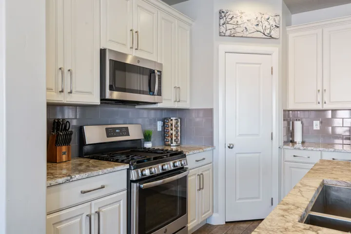 Well-appointed kitchen featuring a stainless steel gas range, coordinating stainless steel microwave, light-toned cabinetry, gray subway tile backsplash, and stone countertops