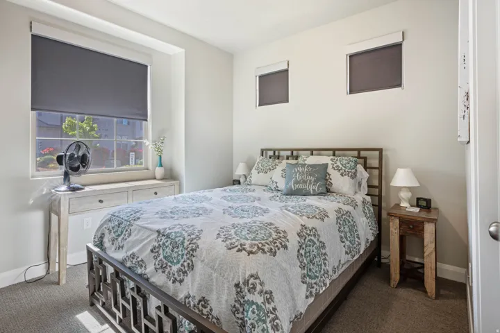 Carpeted bedroom featuring a large window with roller shade, two additional high windows with roller shades, and light-toned wall paint
