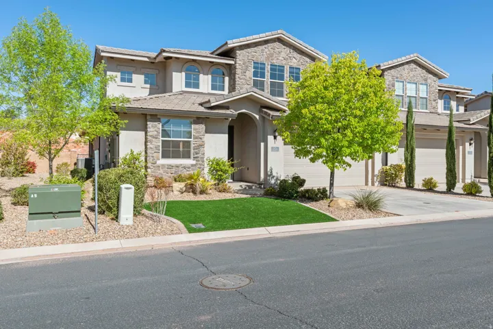 Stucco and stone exterior featuring multiple arched windows, a two-car garage, and low-maintenance landscaping with artificial turf