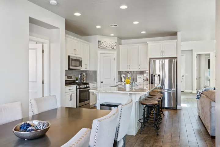 Open-concept kitchen featuring white cabinetry, stainless steel appliances, a multi-level island with seating, and wood-finish flooring