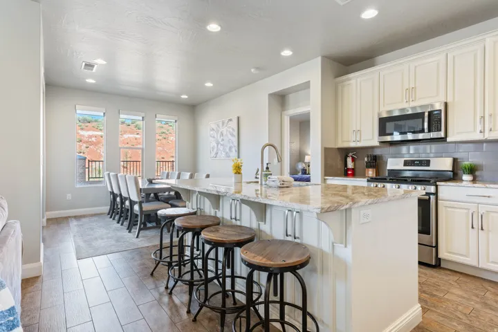 Open-concept kitchen and dining area featuring a spacious island with a stone countertop, white cabinetry, stainless steel appliances, and wood-finish flooring