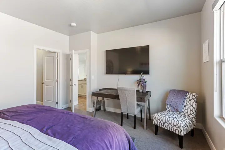 Bedroom featuring light gray walls, built-in wall-mounted television, and a window with blinds