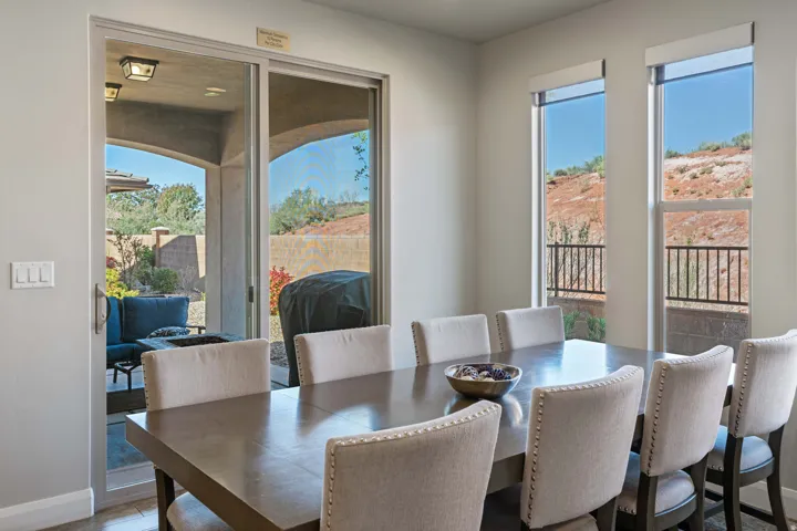 Bright dining area featuring a sliding glass door to an outdoor patio, multiple windows with desert scenery, and light-colored walls