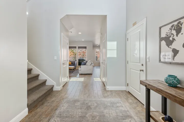 Entryway featuring wood-finish flooring, light grey wall paint, white trim, and a carpeted staircase