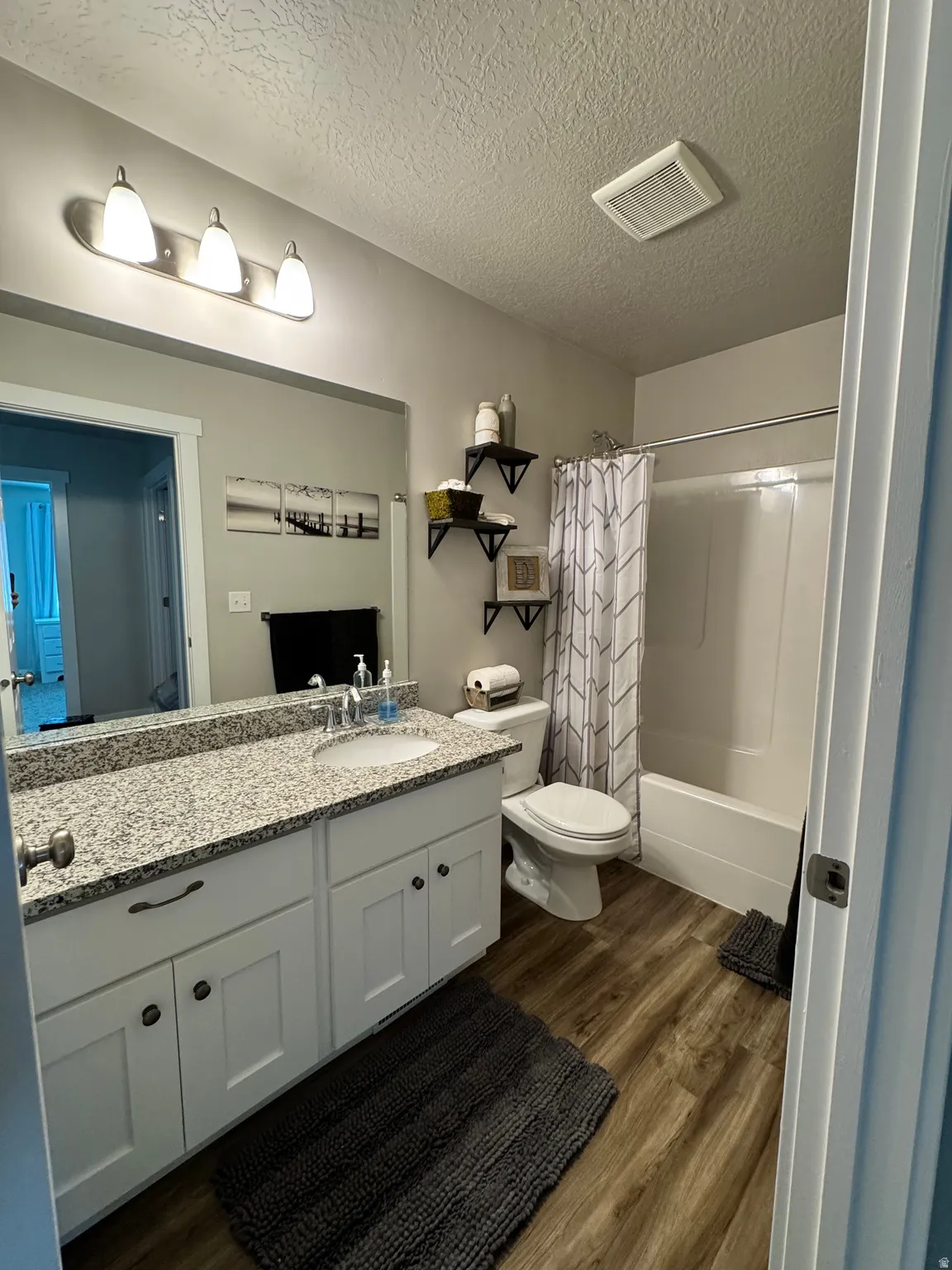 Bathroom featuring a single-sink vanity with granite countertop, white cabinetry, wood-finish flooring, and a shower-tub combination