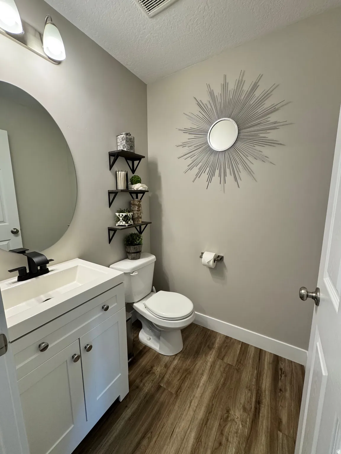 Bathroom featuring a white vanity with integrated sink, black single-handle faucet, and wood-finish flooring