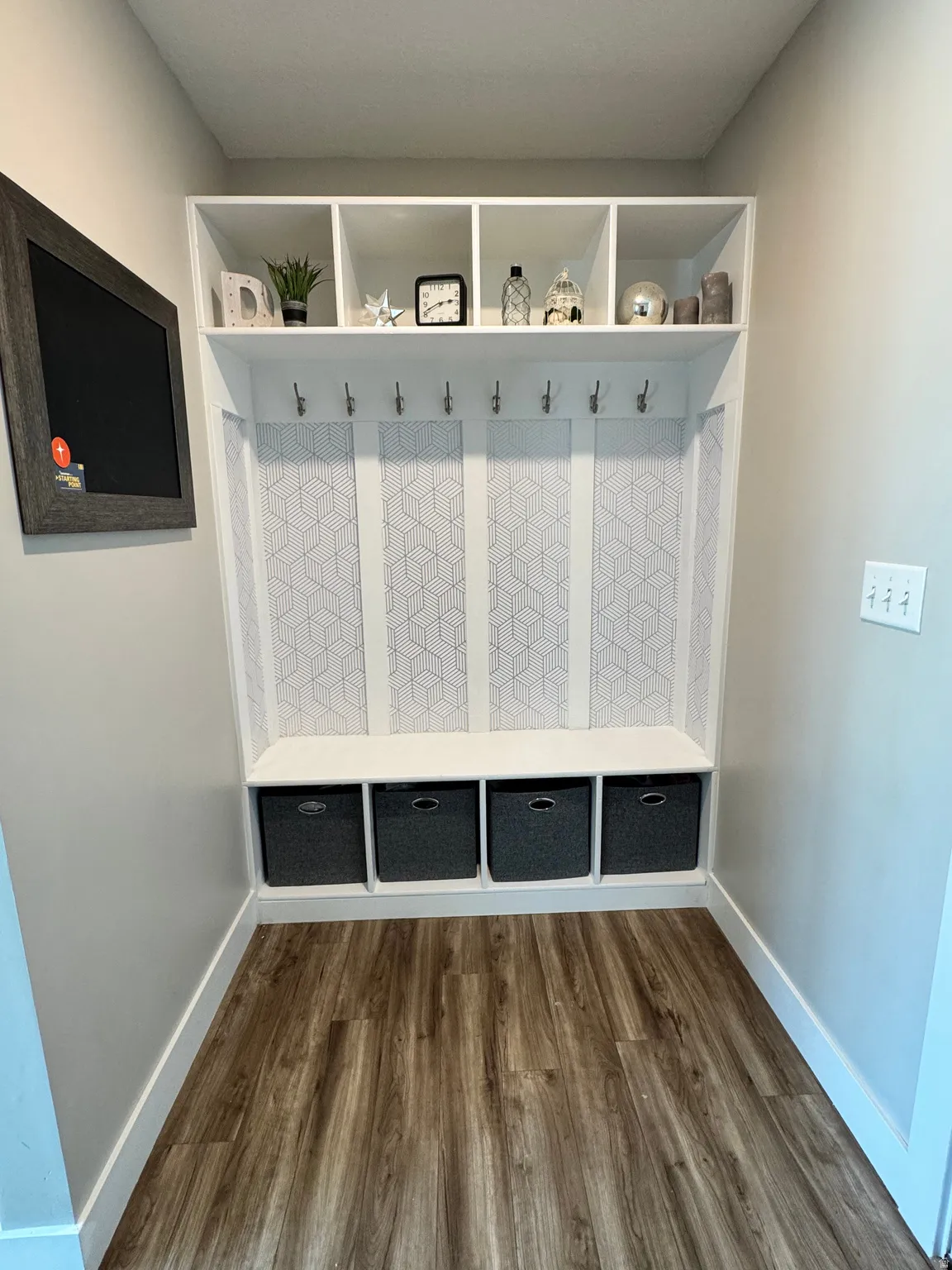 Built-in mudroom bench with cubbies, white upper shelving, wall-mounted hooks, and wood-finish flooring