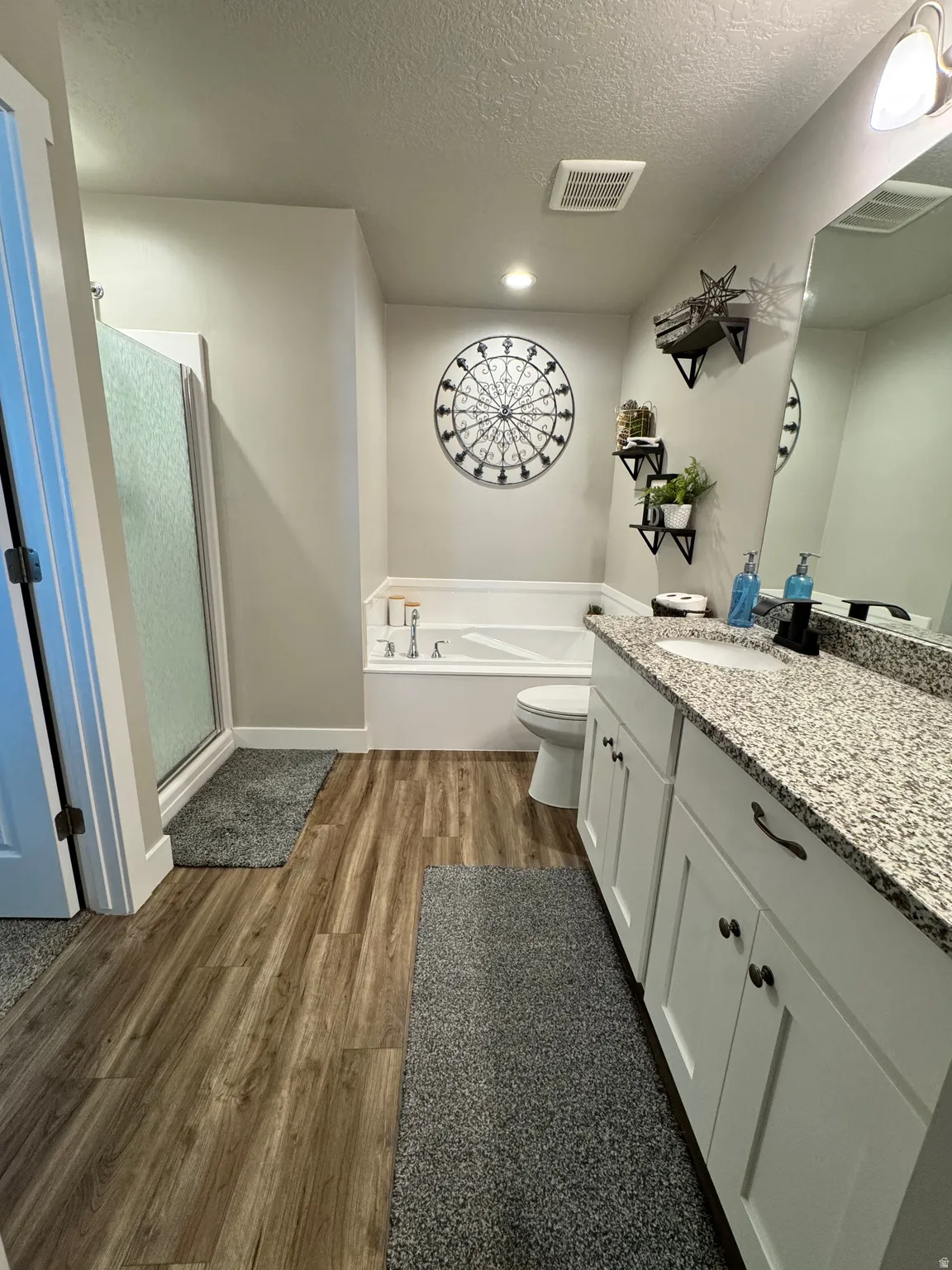 Master Bathroom featuring a double vanity with stone countertops, a full-size tub, a stand-up shower with a glass enclosure, and wood-finish flooring
