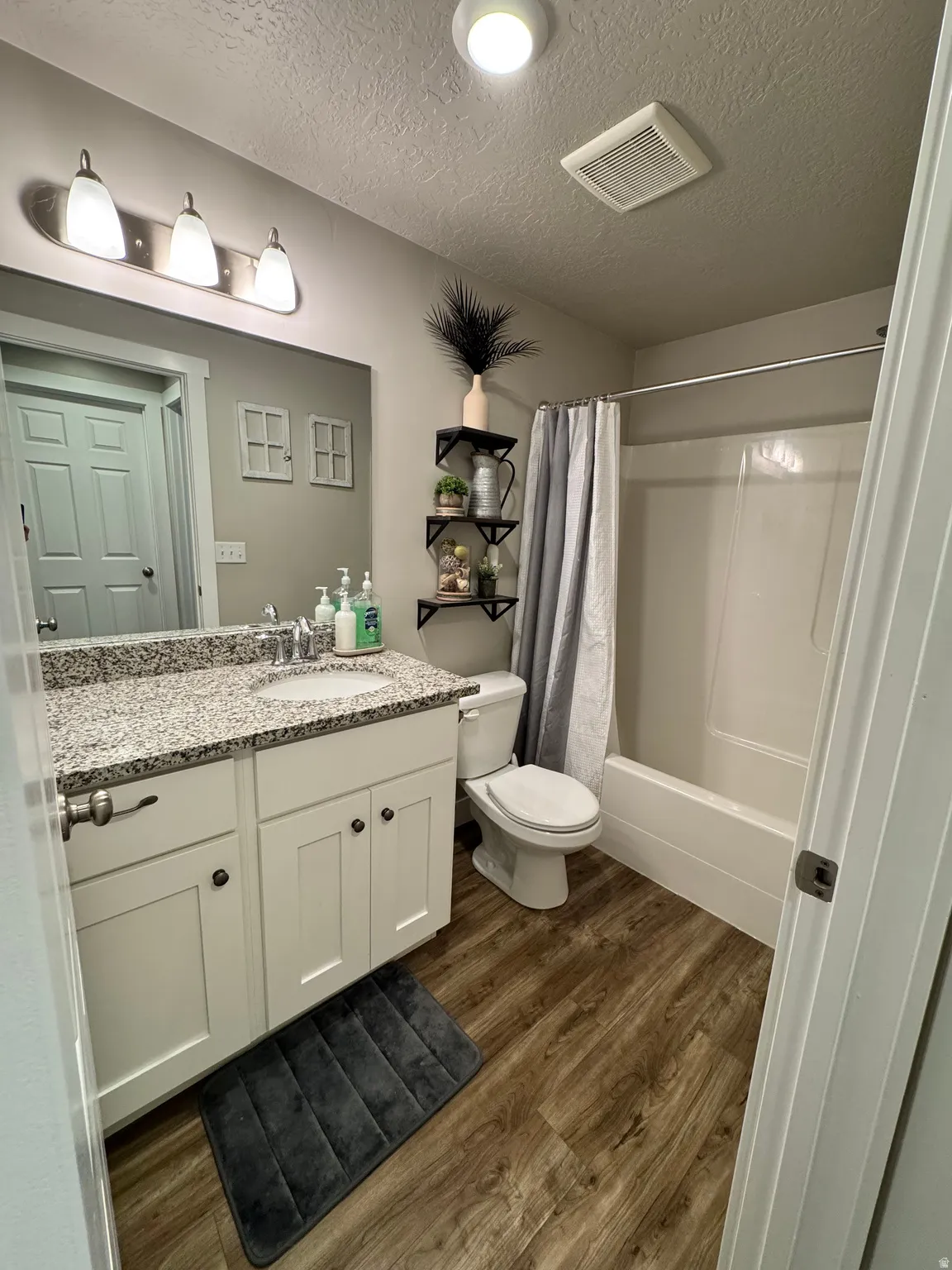 Bathroom featuring a single vanity with a granite countertop, white cabinetry, and wood-finish flooring