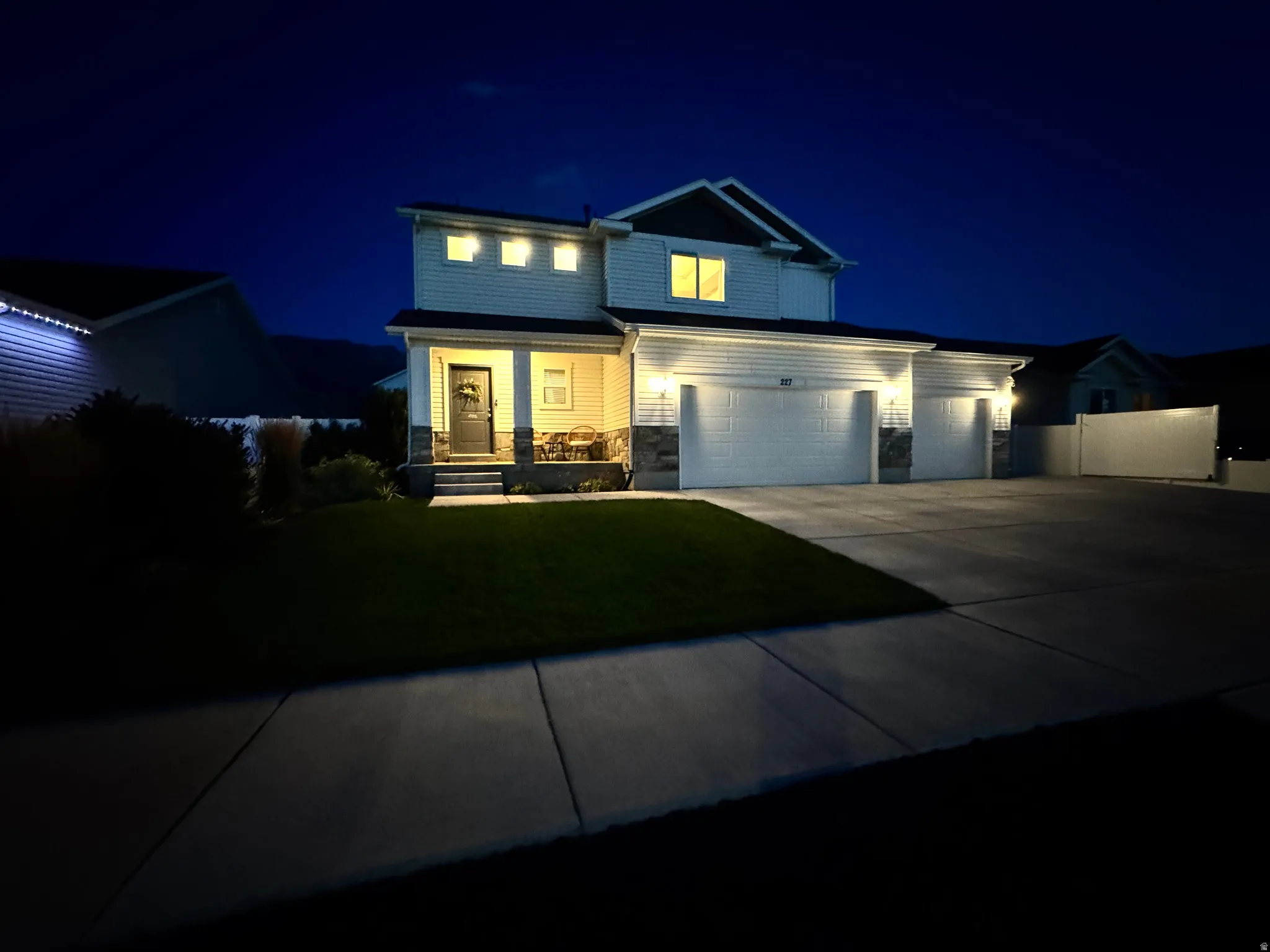 Two-story exterior with white siding and stone accents, featuring a covered front porch, a triple-bay garage with individual doors, and a manicured lawn