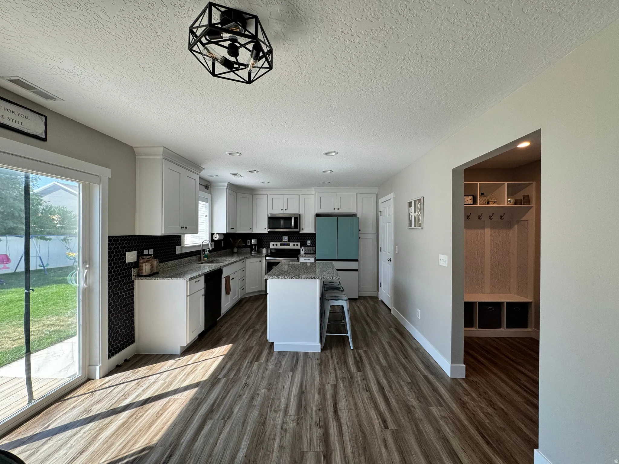 Open-concept kitchen featuring white cabinetry, light-toned countertops, and a black hexagonal tile backsplash