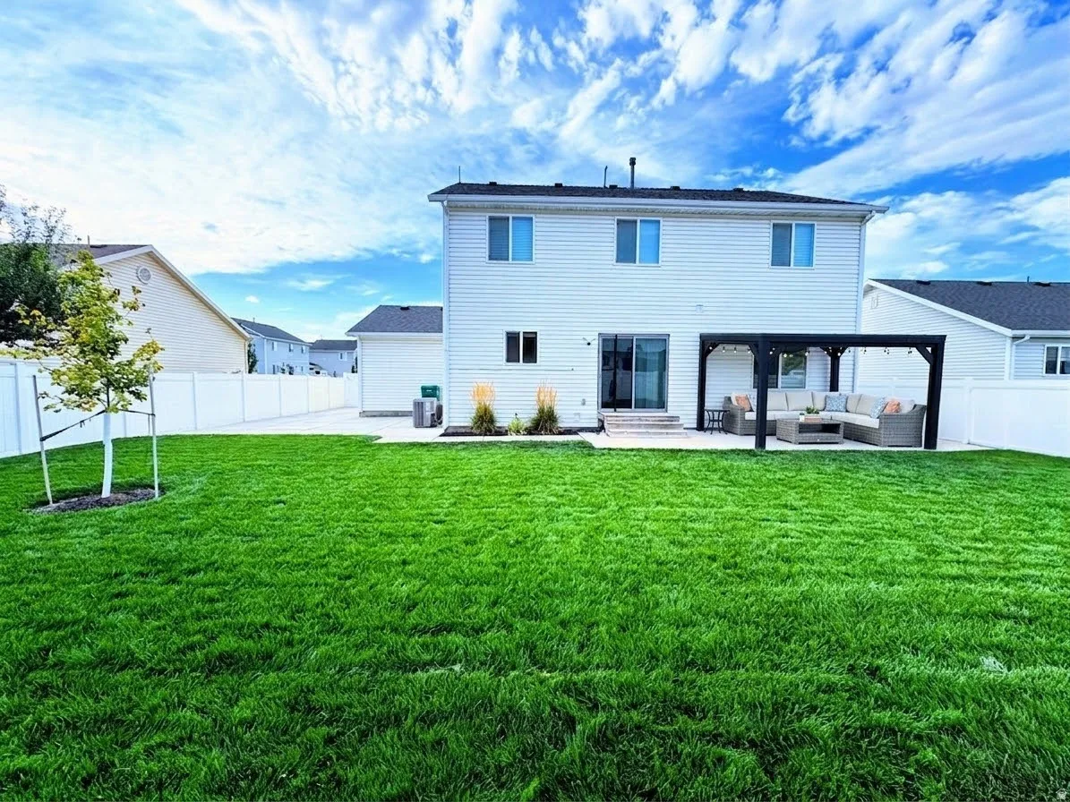 Expansive rear yard featuring green lawn, a white privacy fence, a concrete patio, and a dark-finish pergola