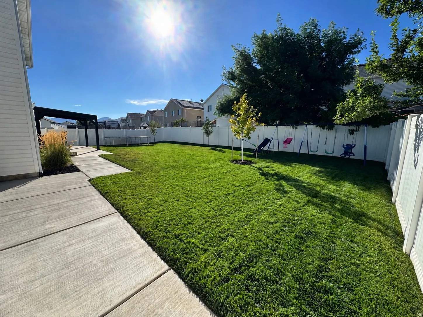 Expansive backyard featuring a lush green lawn, full privacy fencing, and a modern black pergola