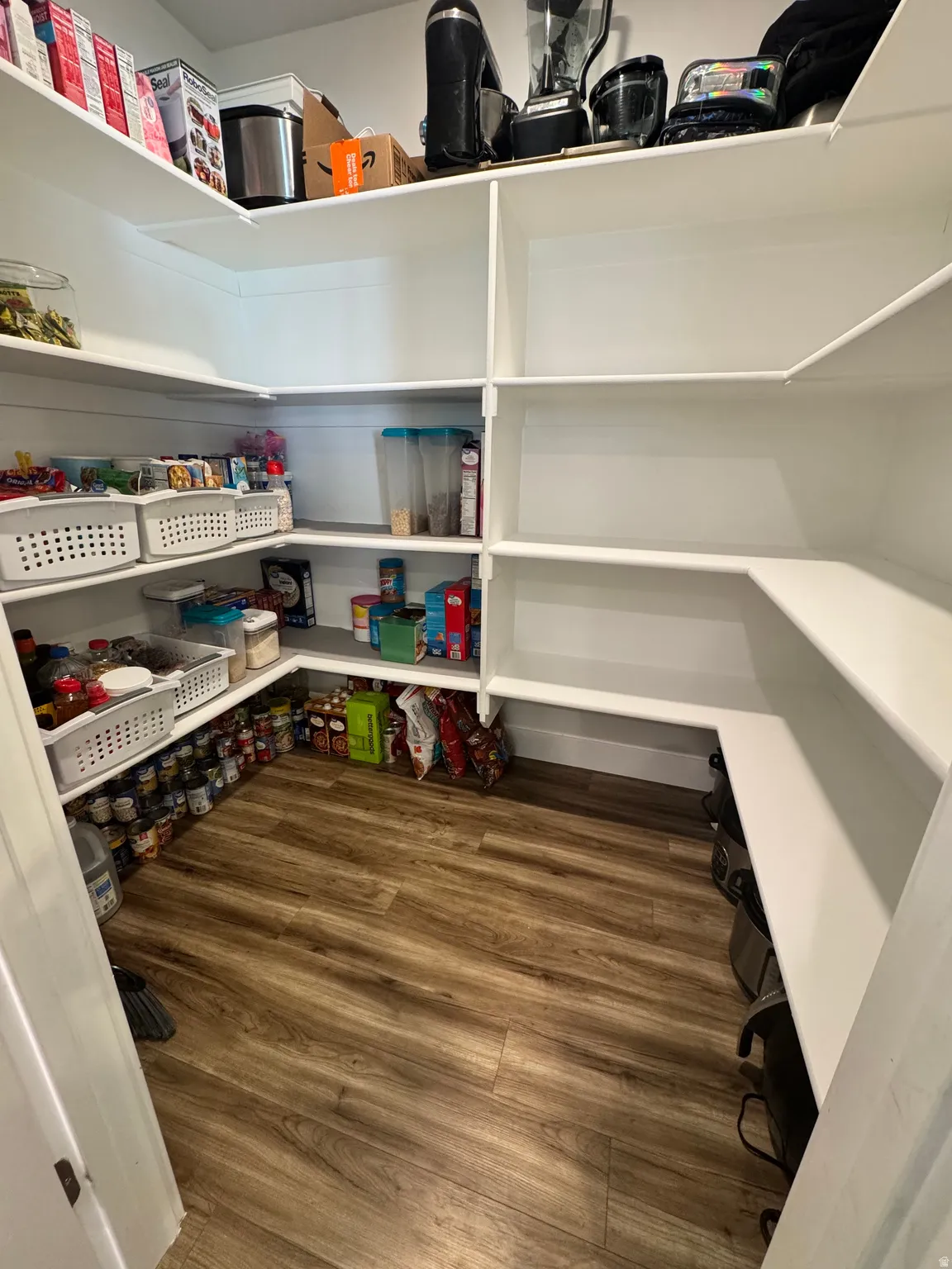 Walk-in pantry featuring extensive white shelving, wood-finish flooring, and ample storage capacity