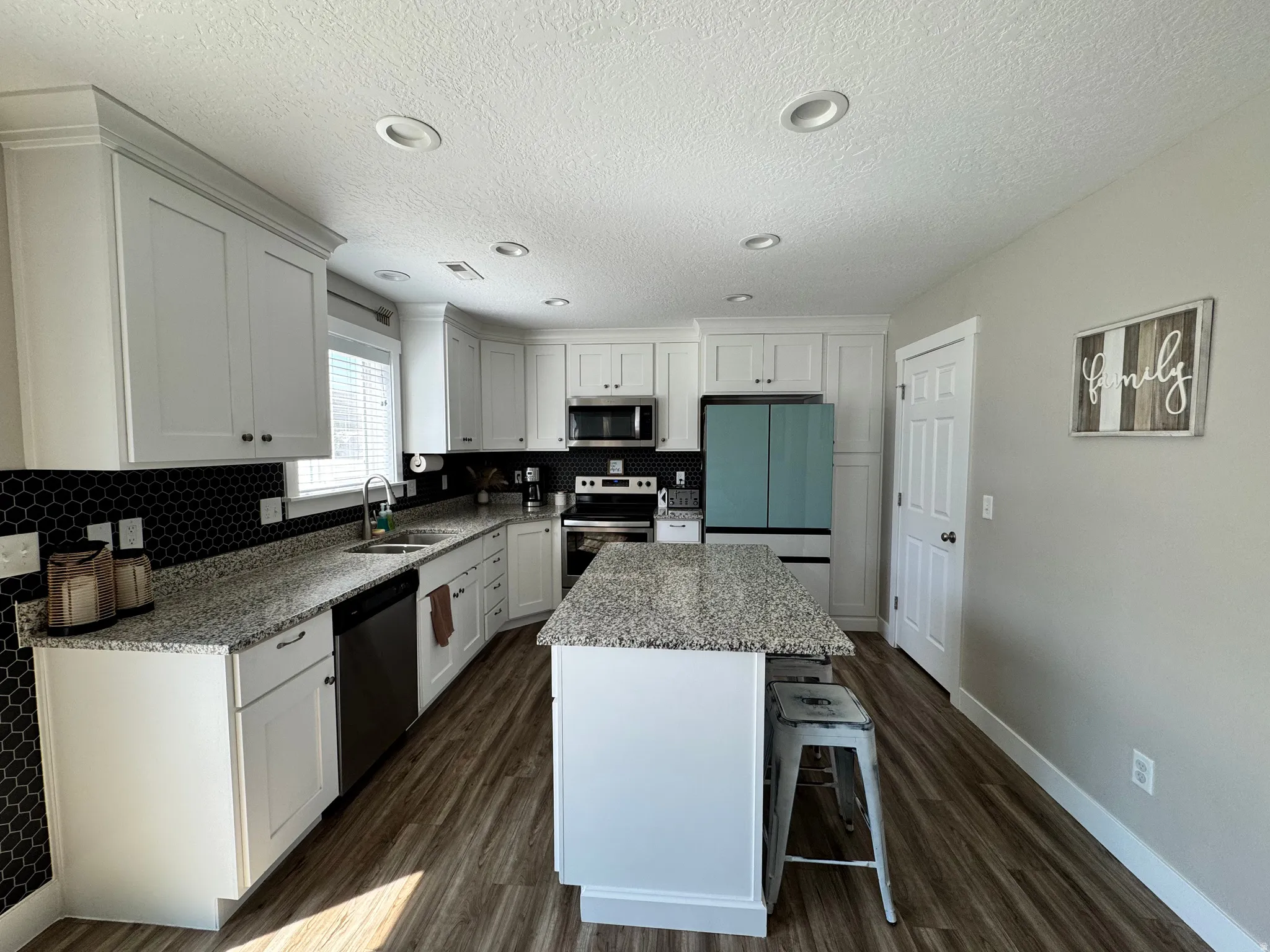 Bright kitchen featuring white shaker cabinetry, granite countertops, and a black honeycomb tile backsplash