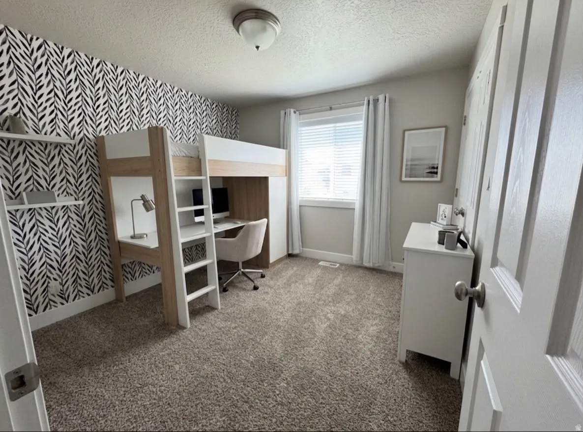 Textured accent wall, neutral carpeting, window with blinds and drapes, ceiling-mounted light fixture, white interior door.  AI enhanced furniture.