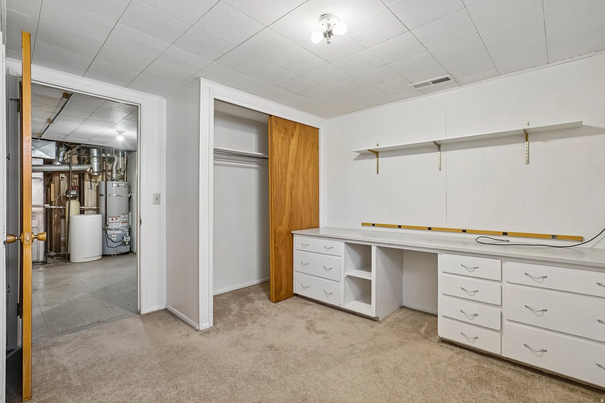 Carpeted room featuring a built-in white desk with drawers, white shelving with brass brackets, and a closet with wood-finish sliding doors